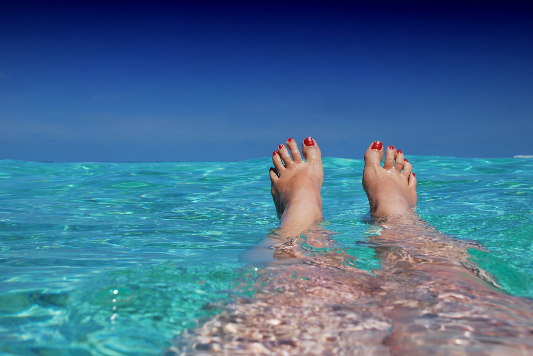 Toes with red nail polish peeking out of blue tropical waters
