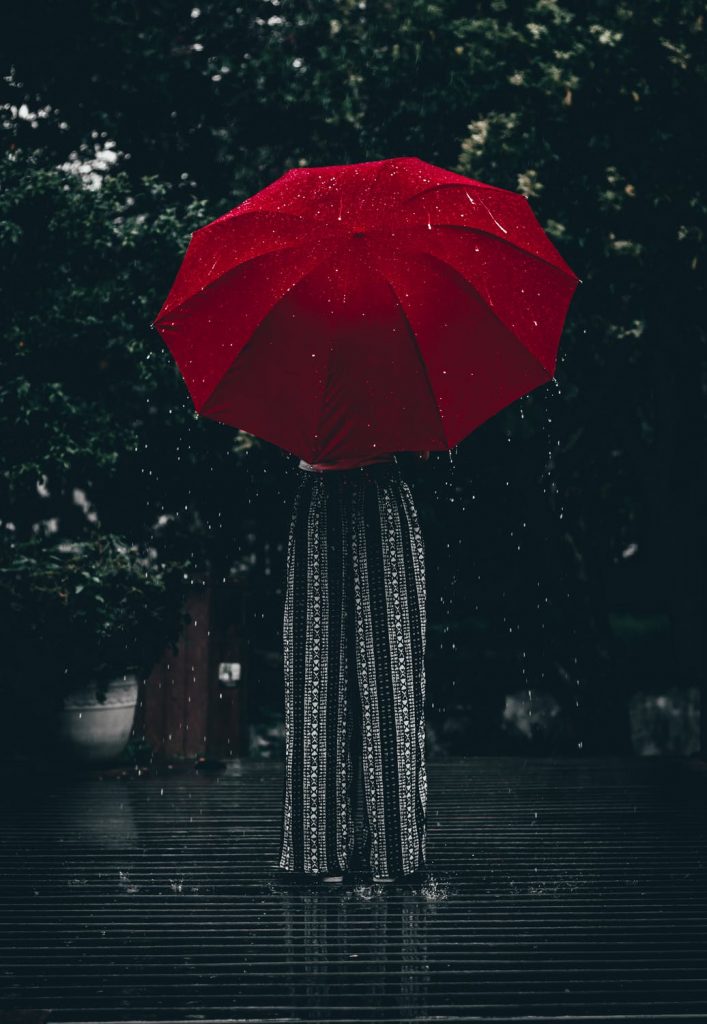 Woman in long printed pants being hidden by super large red umbrella