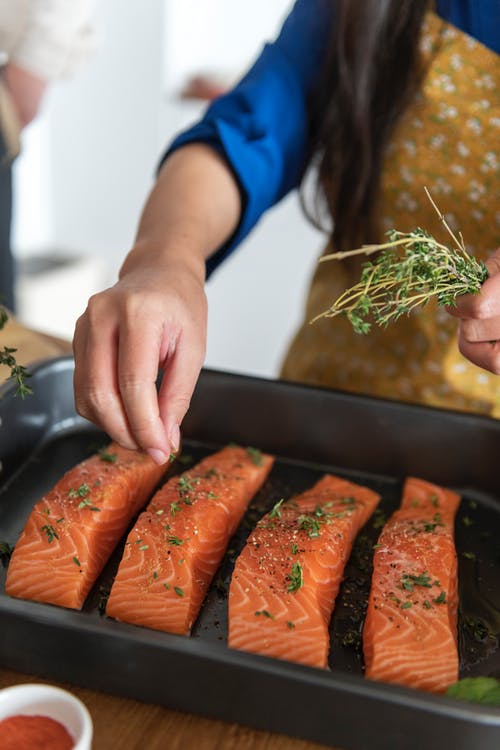 Person sprinkling parsley on to uncooked salmon in a baking dish