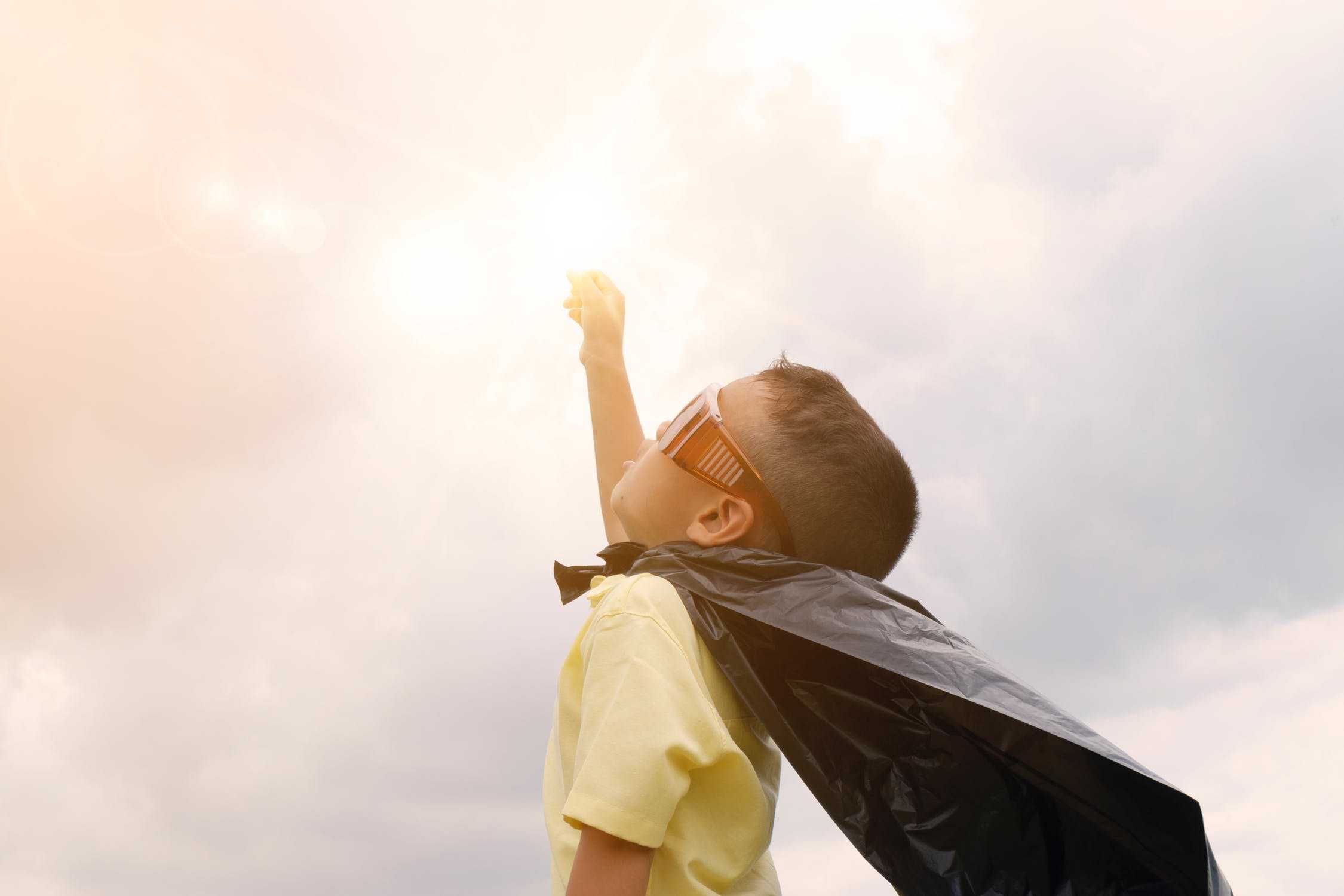 Boy in cape with arm raised being bold in setting goals