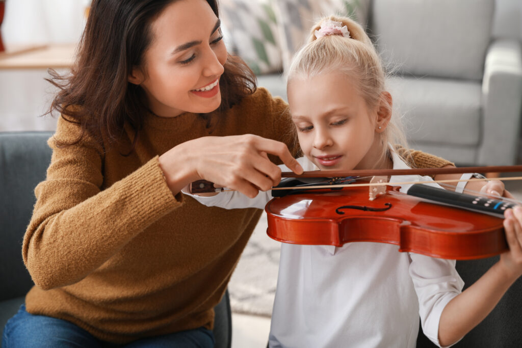 How to Increase Your Income by Giving Private Music Lessons. Woman teaching young girl how to hold violin bow