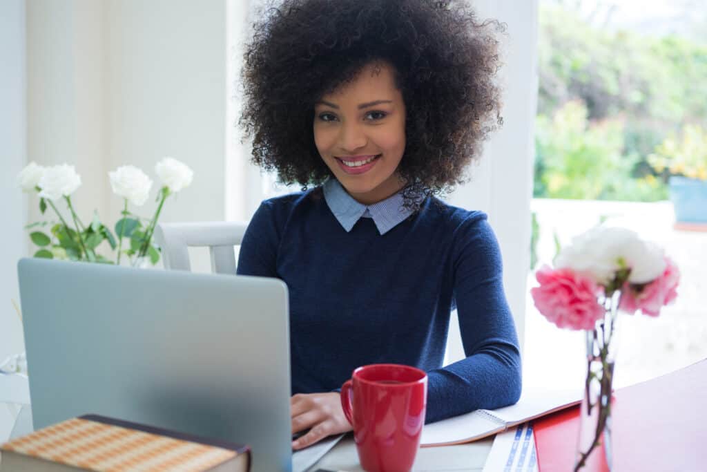 Online Proofreading Jobs woman in dark blue sweater looking happy at computer